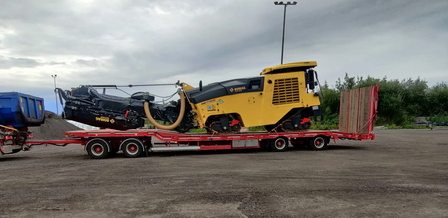 Sininen Nehvosen lavettiauto kuljettaa pyöräkuormaajaa iltavalossa